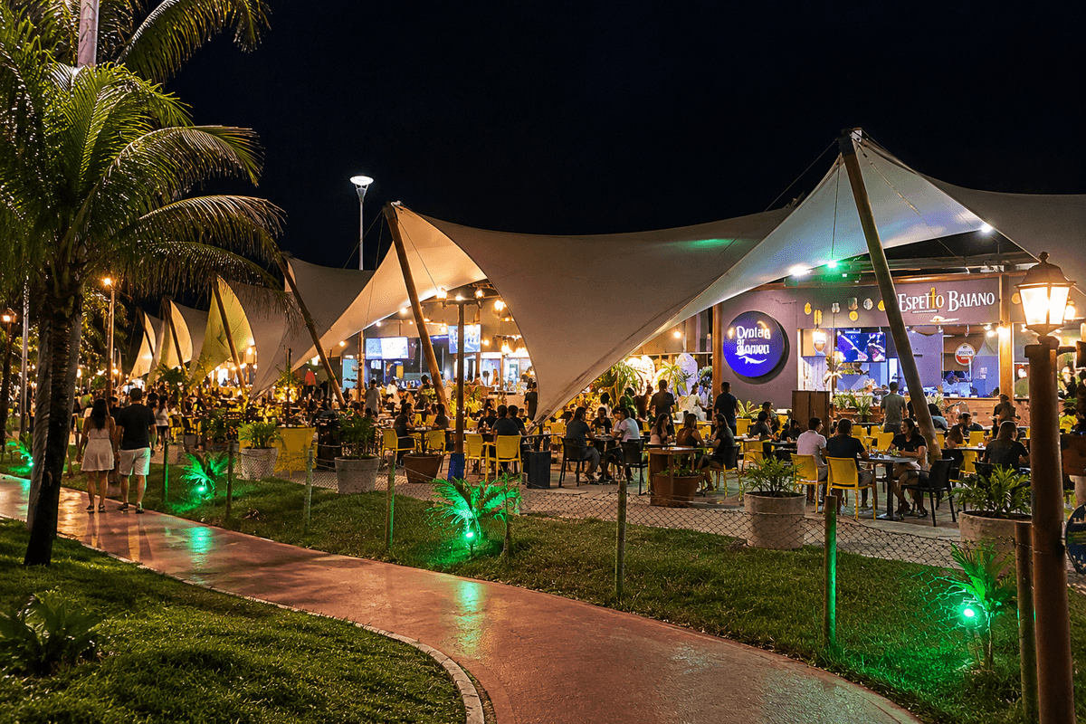 Vila Caramuru en Rio Vermelho por la noche, con cubiertas tensadas iluminadas, mesas al aire libre, vegetación tropical y gente cenando y paseando por el complejo.