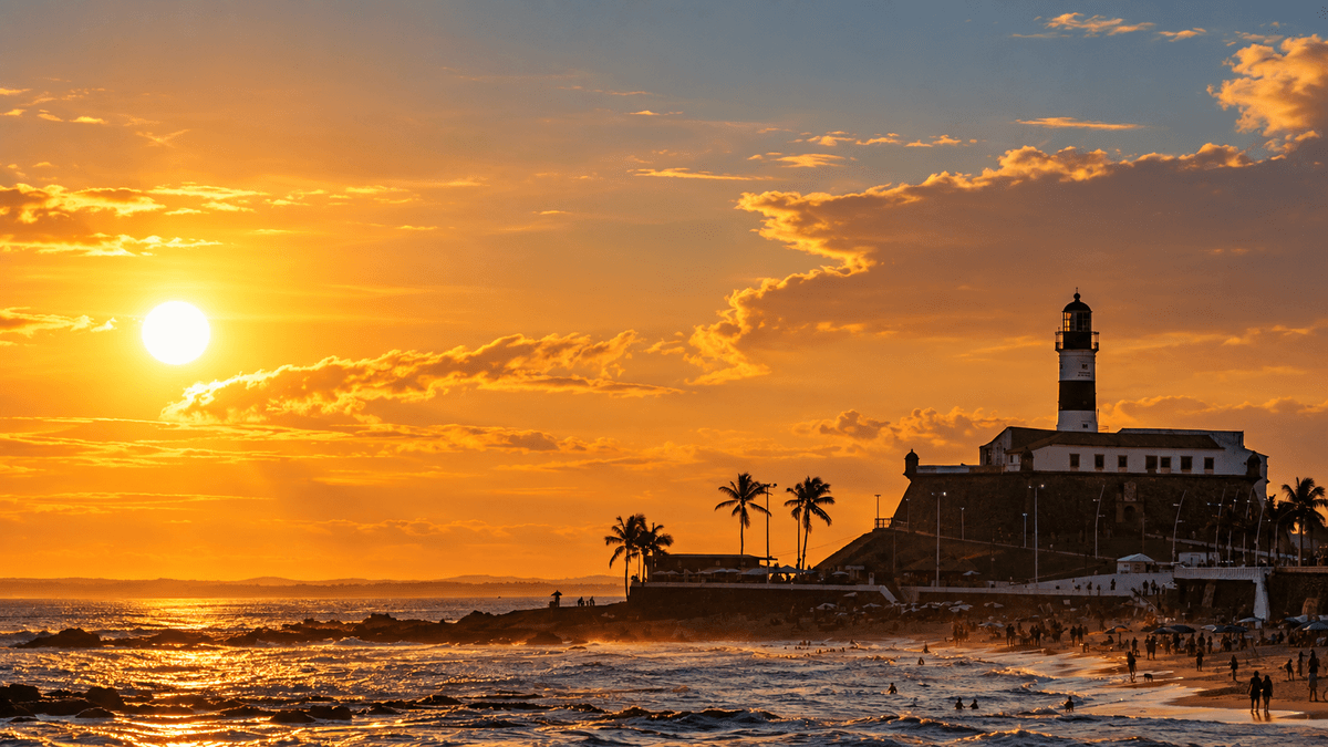 El Farol da Barra recortado sobre la playa y el océano Atlántico durante un atardecer dorado en Salvador.